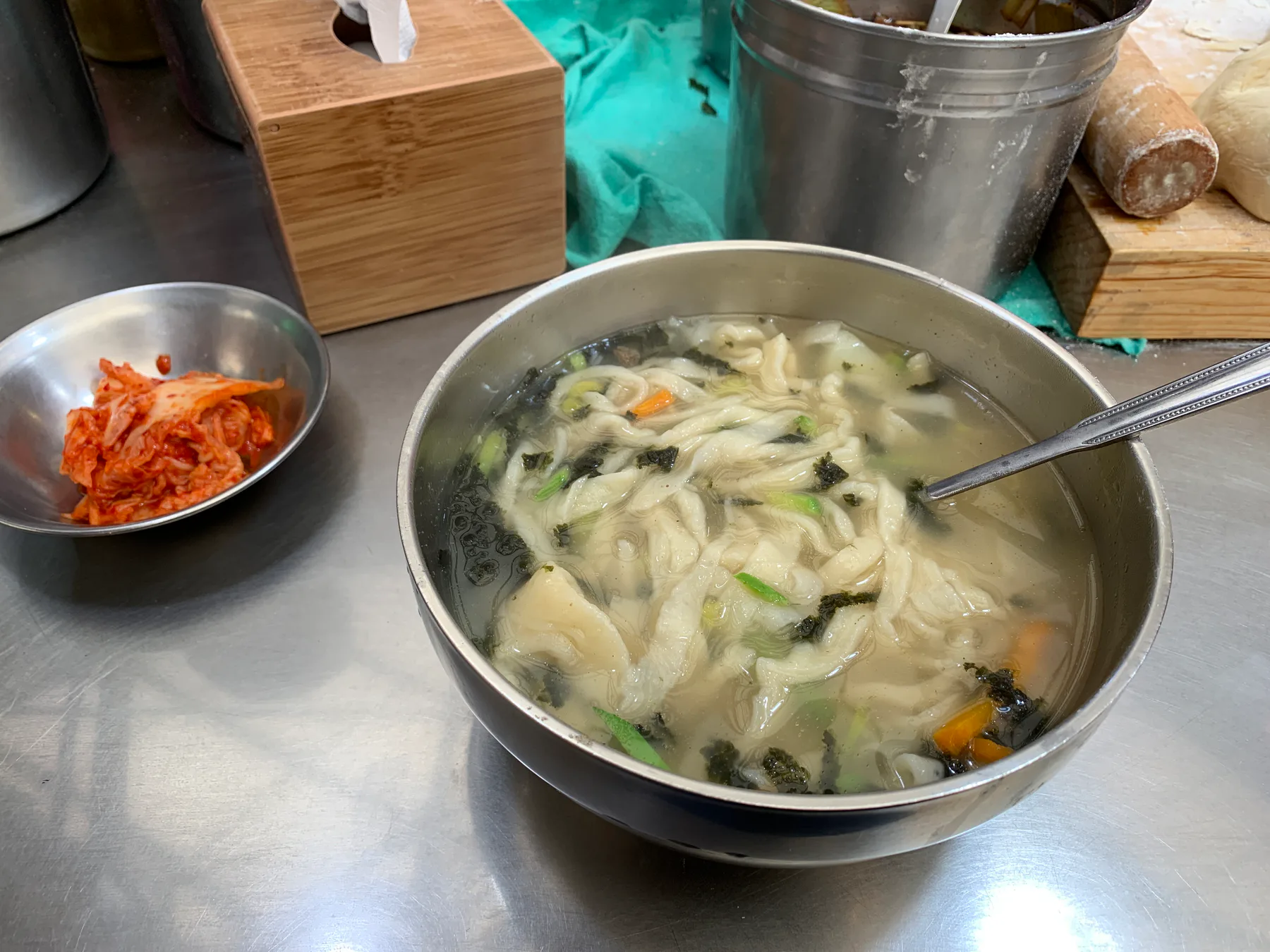 A bowl of market noodle soup on a stainless counter in Gwangjang Market.