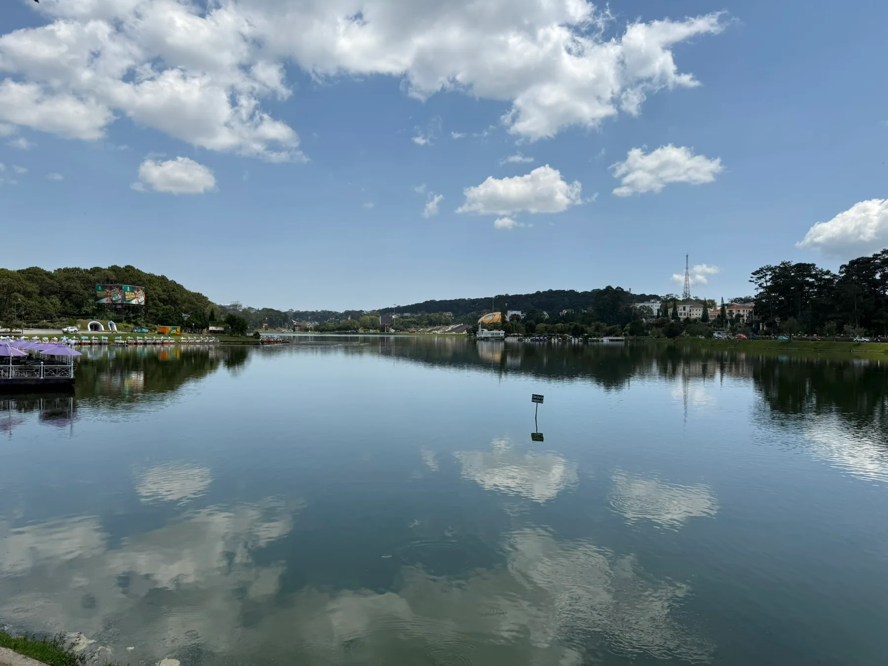 A calm lake in Da Lat reflecting clouds and green hills.