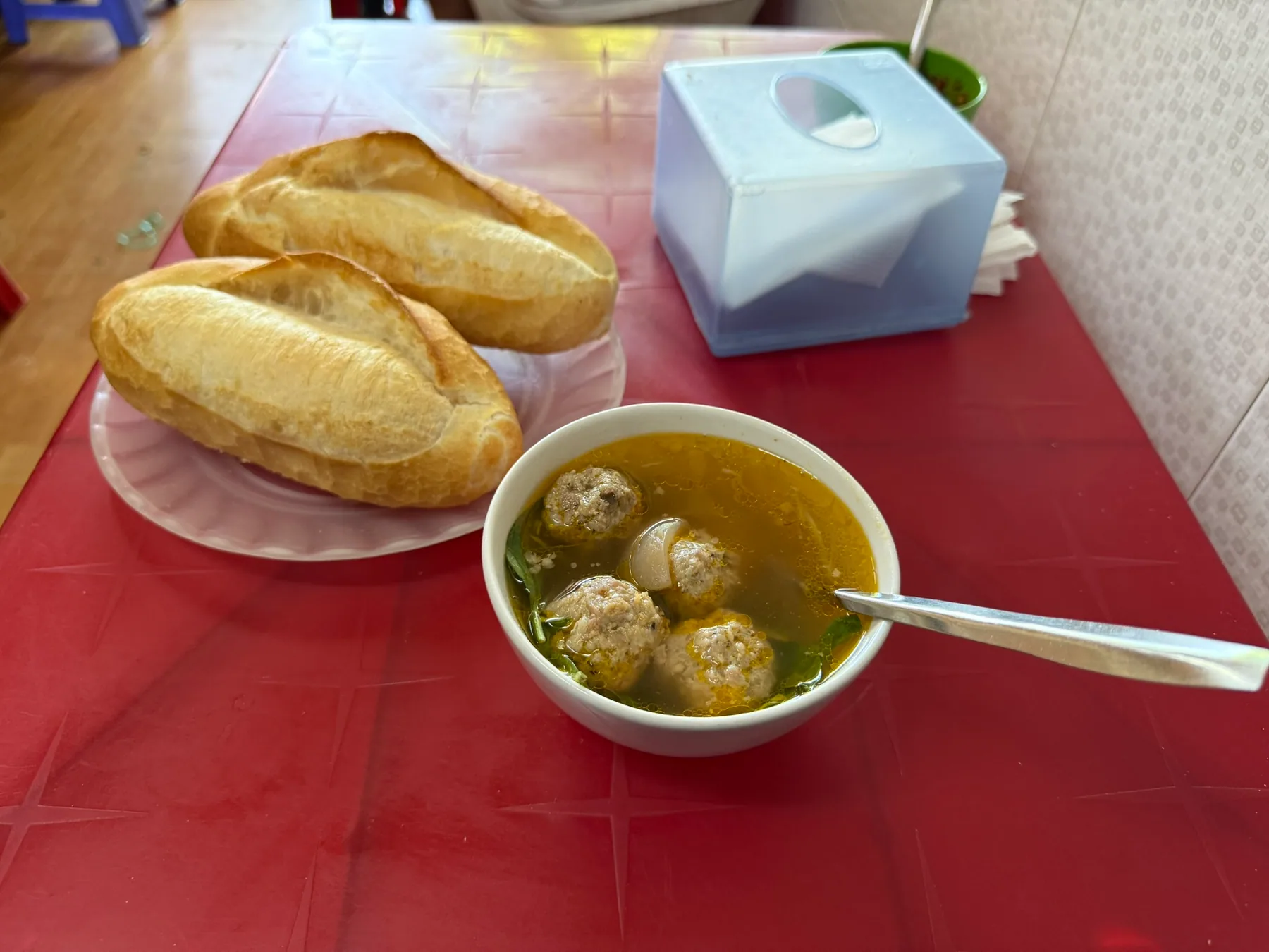 A bowl of xíu mại with bread on a small red table in Da Lat.