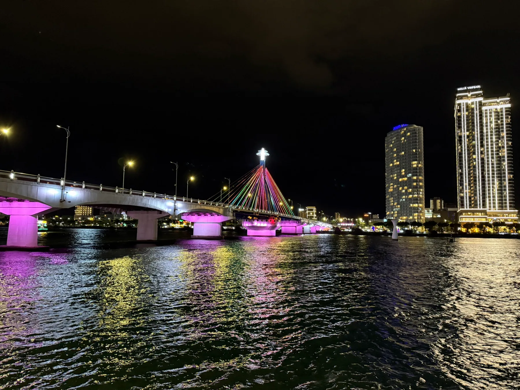 The Sông Hàn Bridge glowing at night across the water in Da Nang.