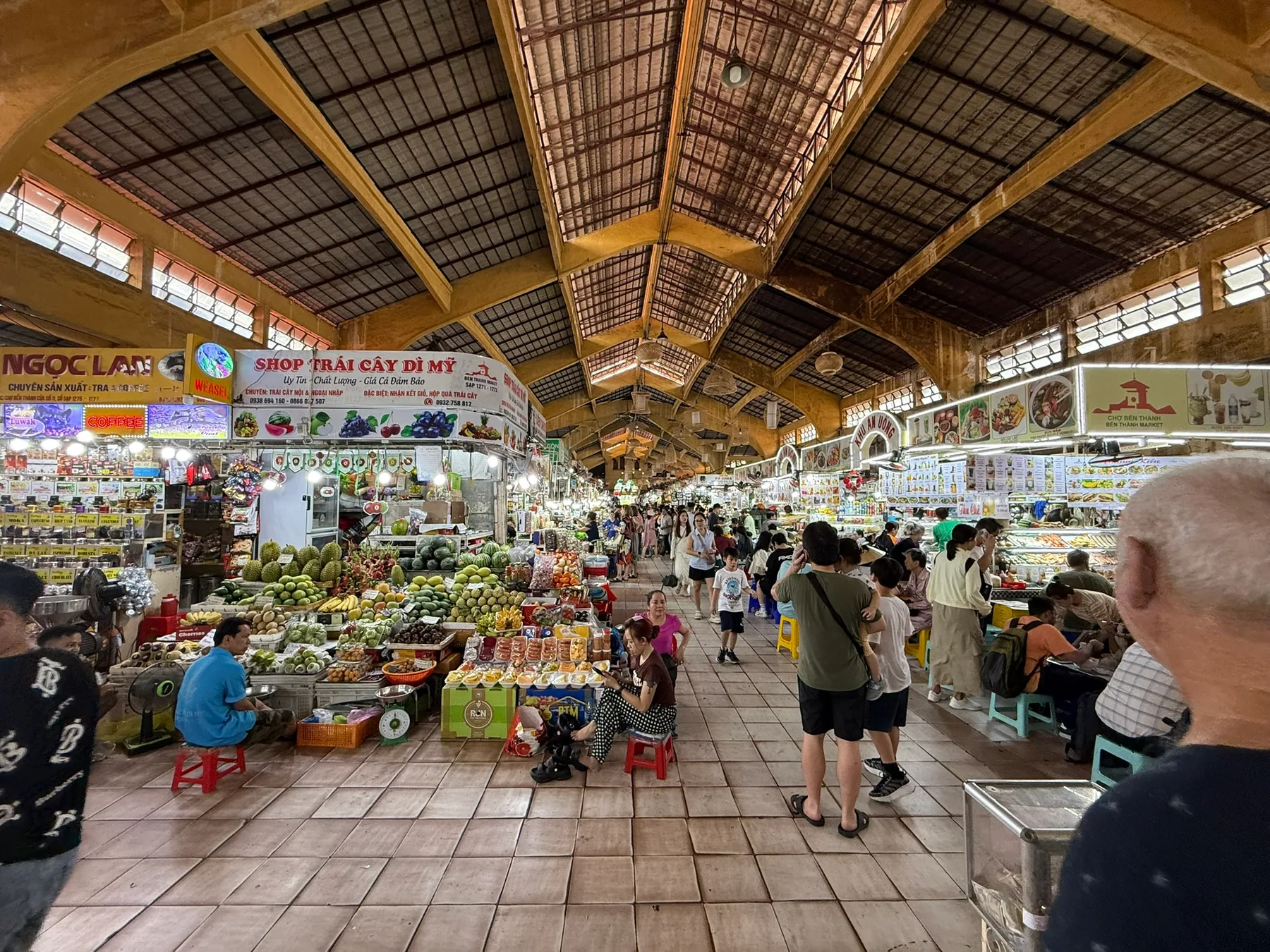 A covered market in Ho Chi Minh City with produce stalls and people moving through the aisles.