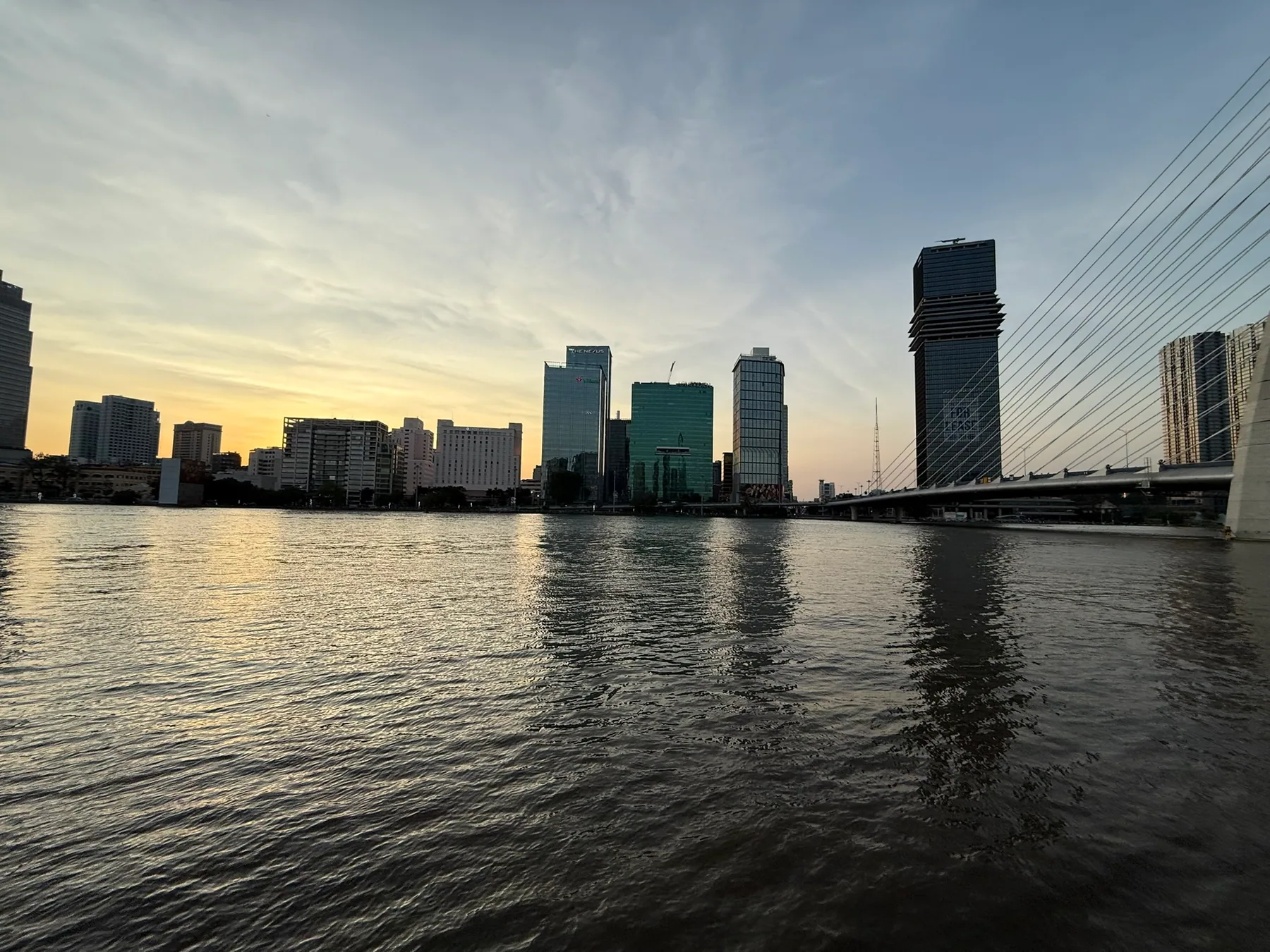 The Saigon River at dusk with city buildings and bridge cables across the water.