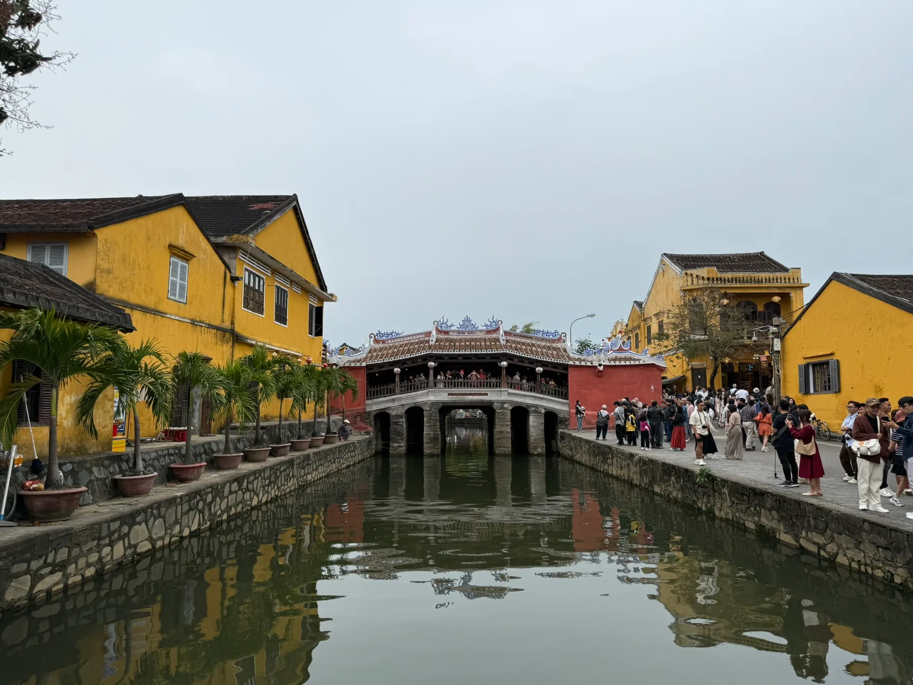 The Old Town riverfront in Hội An with yellow buildings and a bridge reflected in the water.