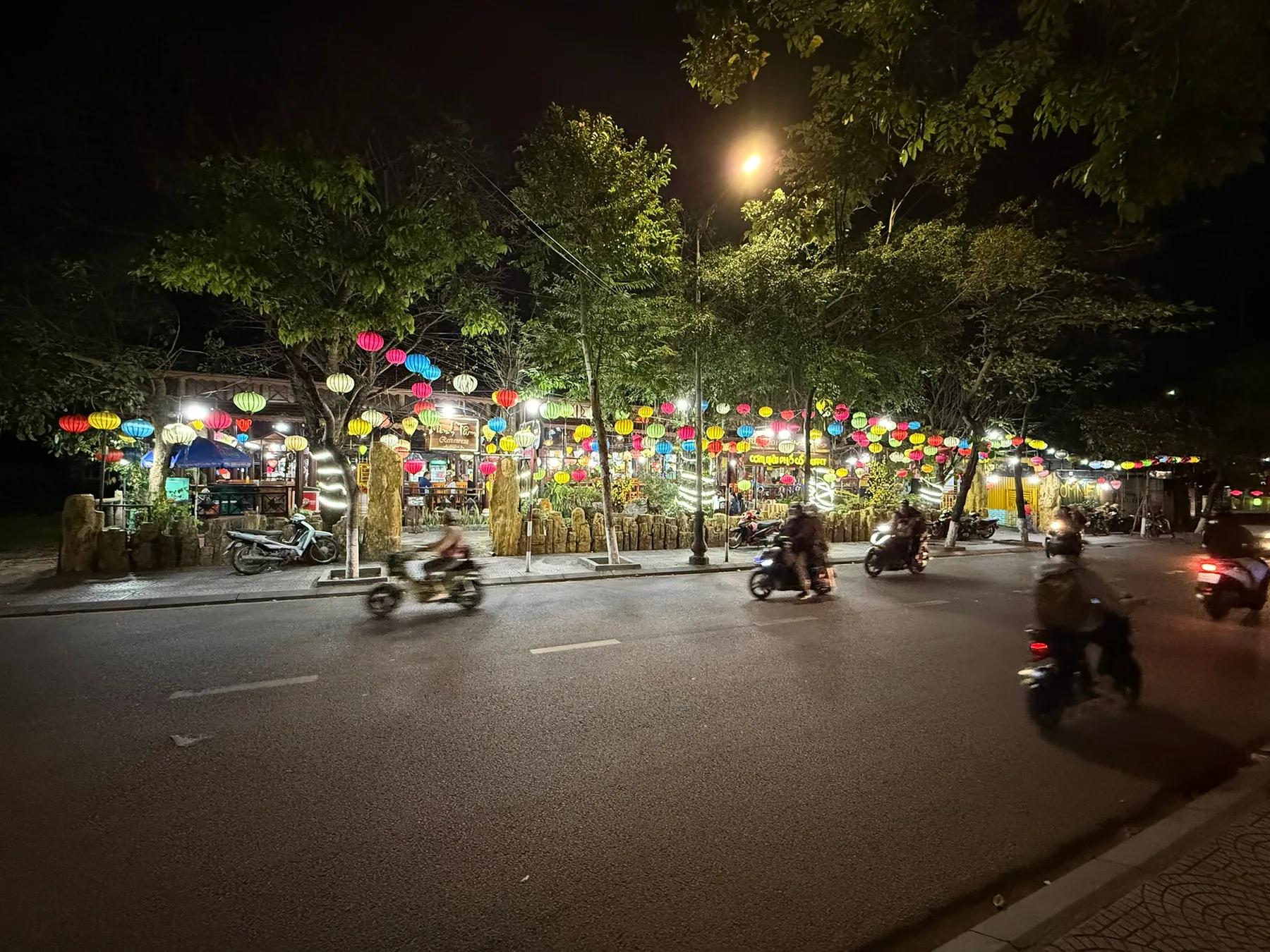 Hội An at night with lanterns and scooters moving along the street.
