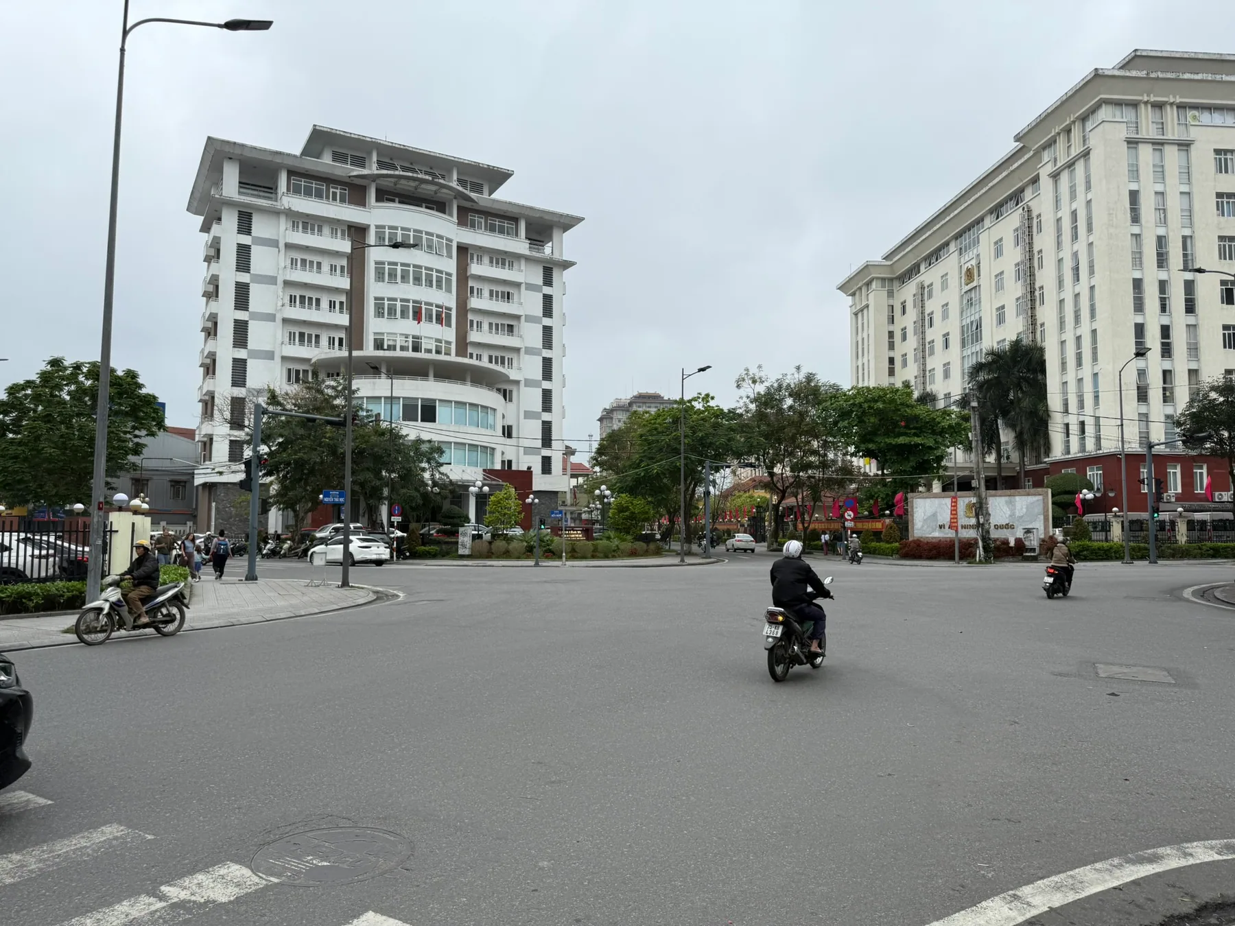 A Huế street with scooters and pale buildings under a gray sky.